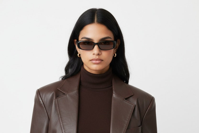 Woman wearing a brown leather jacket and turtleneck against a white background with black sunglasses fashoned with a brown lens